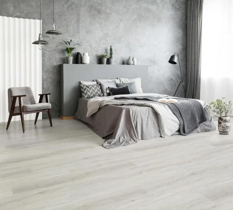 Modern bedroom featuring RoyalStep Laminate 12mm flooring in Ashen Oak, complemented by a grey accent wall, stylish decor, and natural lighting.