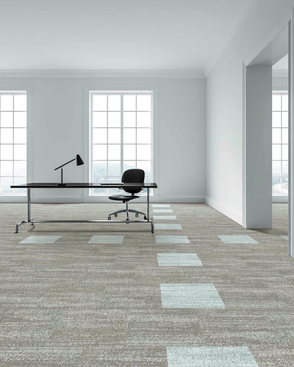 Modern office space featuring Spectre carpet tiles in a textured loop finish, showcasing a blend of grey and light blue squares, with a sleek desk and ergonomic chair under natural light from large windows.