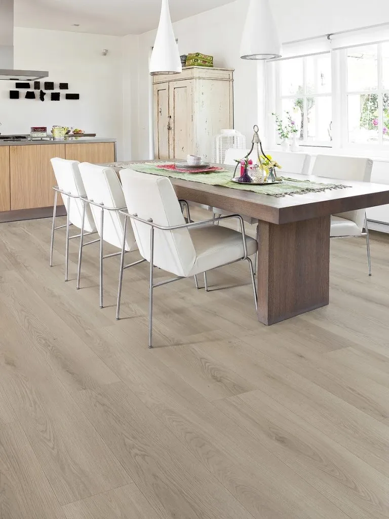Modern dining area featuring Royal 10mm Extreme Fawn Grey hybrid flooring, showcasing light wood grain texture, white chairs, and a wooden table with decorative items.