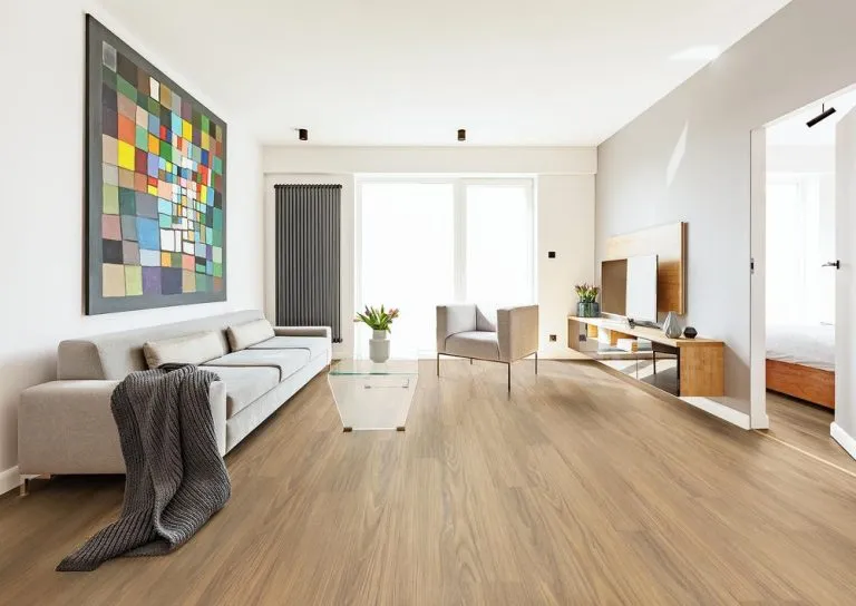 Spacious living room featuring RoyalStep 12mm laminate flooring in Spotted Gum, modern furniture, large windows, and colorful artwork.