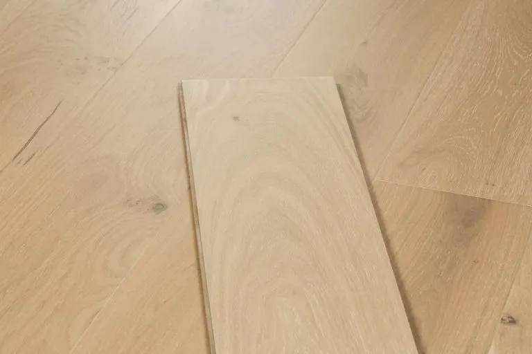 Royal 15/4mm Oak flooring sample in Sandstone color showcasing natural wood grain texture on a light wooden surface.