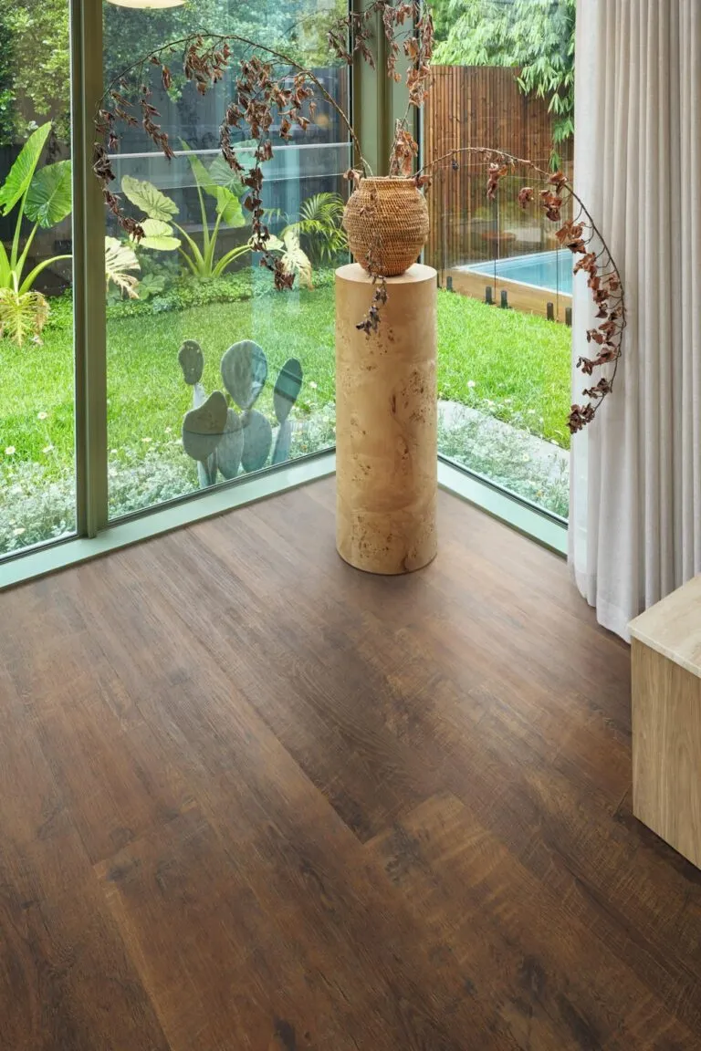 Antique French Oak flooring in a modern interior setting with large windows, featuring a decorative vase on a wooden pedestal and greenery outside.