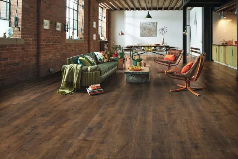 Open-plan living space featuring Antique French Oak flooring, stylish green sofa with colorful cushions, modern wooden chairs, and a rustic coffee table, complemented by exposed brick walls and large windows.
