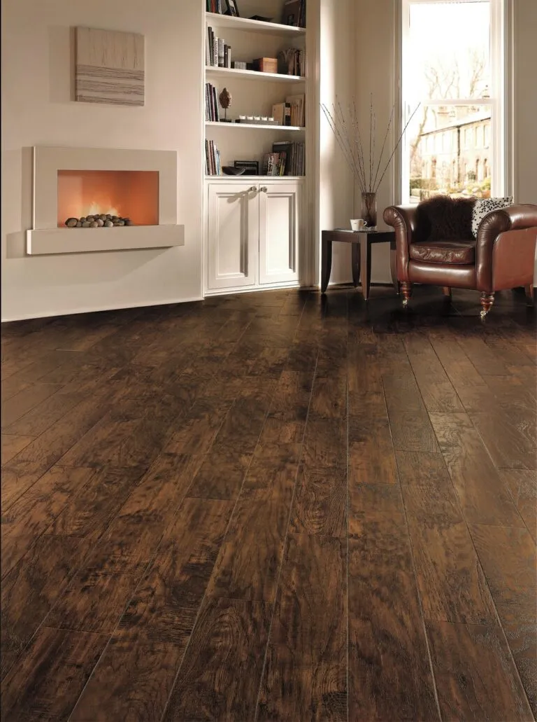 Hickory Peppercorn luxury vinyl flooring in a modern lounge setting, featuring a cozy armchair, sleek fireplace, and stylish bookshelf, showcasing its rich, dark wood appearance and seamless installation ideal for high-traffic areas.