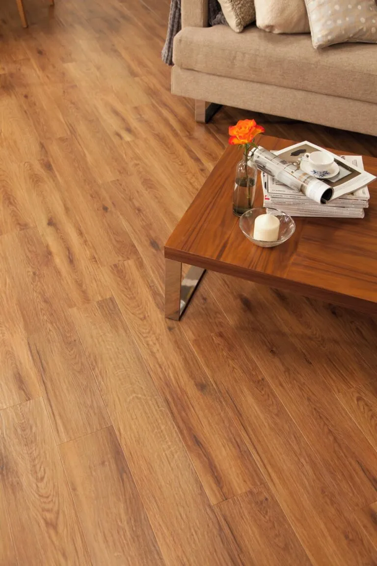 Luxury vinyl flooring in Morning Oak finish, showcasing a warm wood grain texture, complemented by a modern coffee table with decorative items and a cozy living room setting.