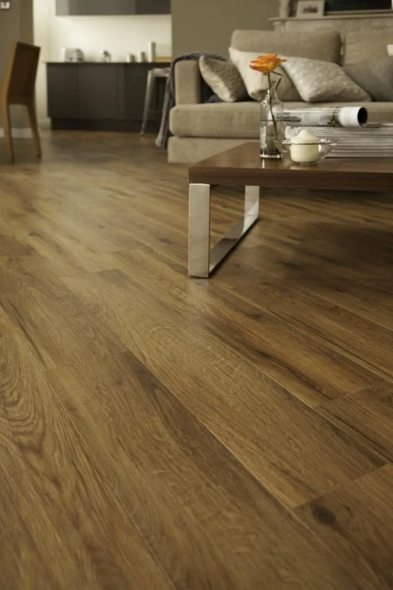 Luxury vinyl flooring in Morning Oak finish, showcasing realistic wood grain texture and warm tones, set in a modern living space with a coffee table and sofa.