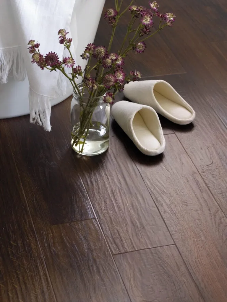 Evening Oak luxury vinyl flooring with a vase of purple flowers and cozy slippers, highlighting a warm and inviting bathroom setting.