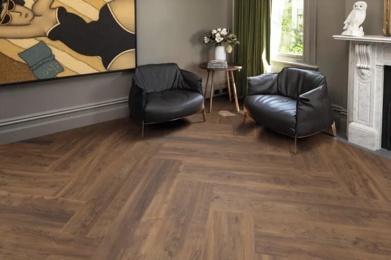Luxury vinyl flooring in Heritage Oak finish, showcasing a stylish living space with two modern black armchairs, a small side table, and elegant decor against a backdrop of herringbone-patterned wood flooring.