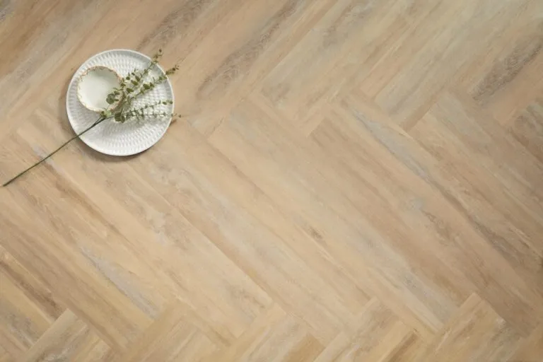Hamden luxury vinyl flooring in herringbone pattern, featuring a light wood finish, accompanied by a decorative plate and greenery, showcasing the elegance and versatility of Karndean's LooseLay Originals collection.