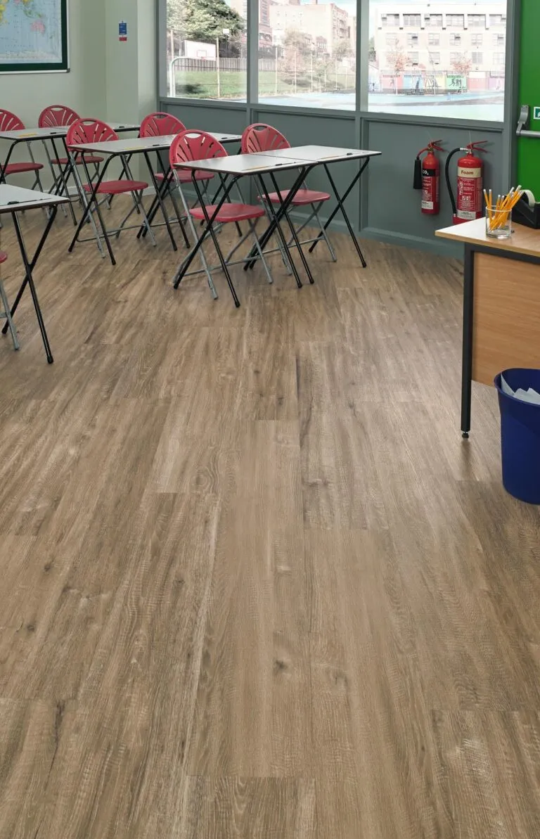 Neutral Oak LooseLay Longboard vinyl flooring in a classroom setting with red folding chairs and desks, showcasing a modern and spacious appearance.