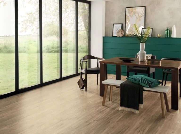 Neutral Oak LooseLay Longboard vinyl flooring in modern dining room setting with large windows, wooden dining table, and decorative plants.
