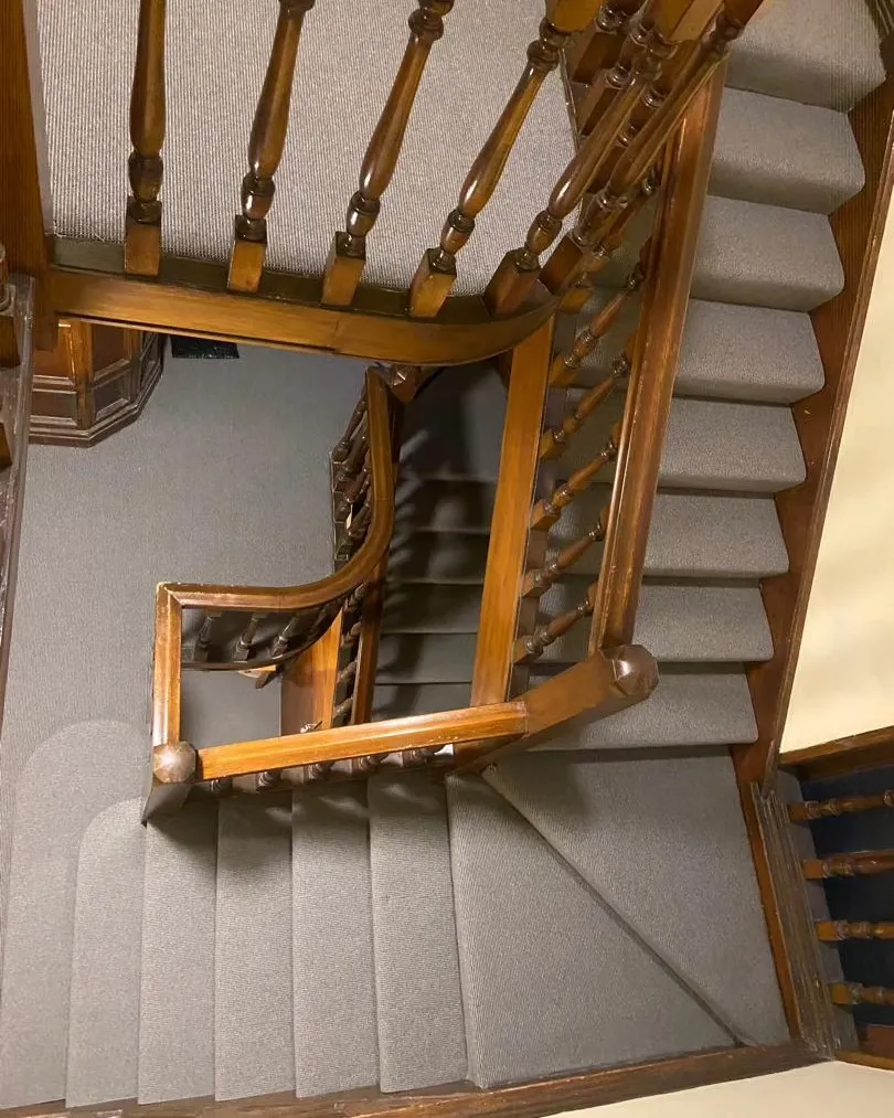 Wooden staircase with a carpet runner, viewed from above, showcasing ornate banister