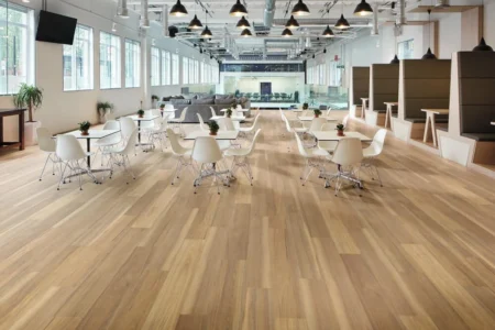 Modern office breakout area featuring Korlok Weathered Spotted Gum hybrid vinyl flooring, with tables and chairs, large windows, and a contemporary design.